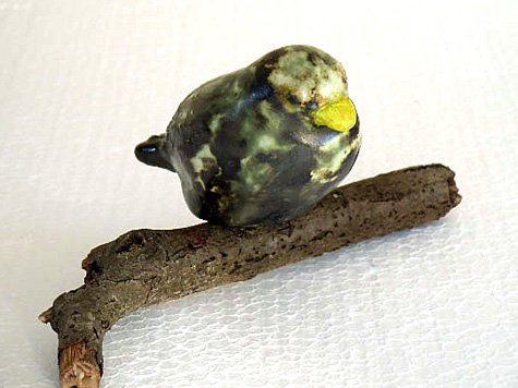Groen-geel keramiek vogeltje miniatuur op houten tak
